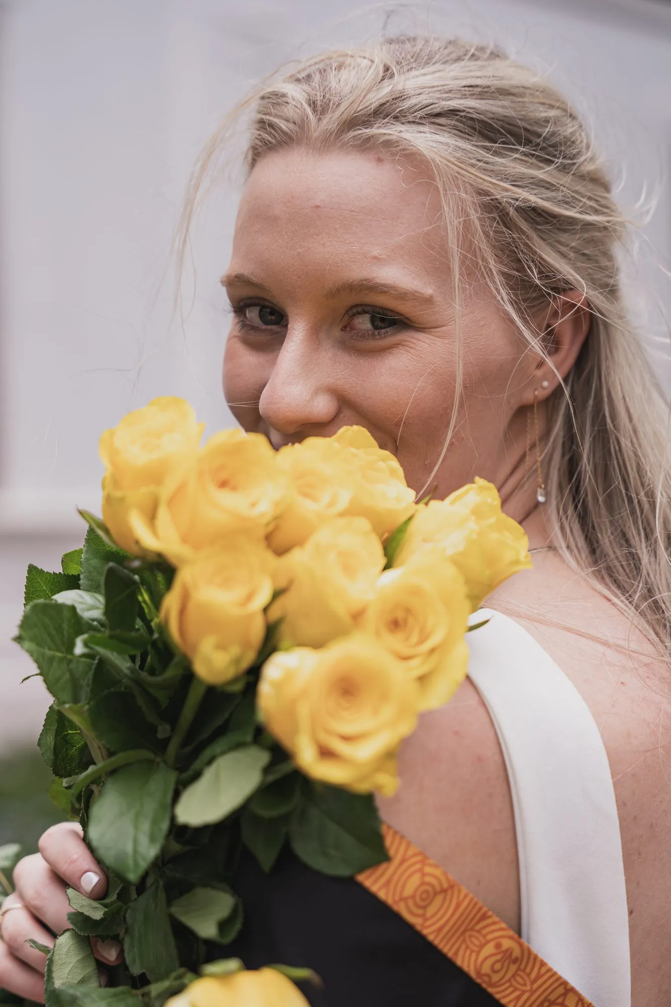 Graduate smiling behind a bouquet of yellow roses